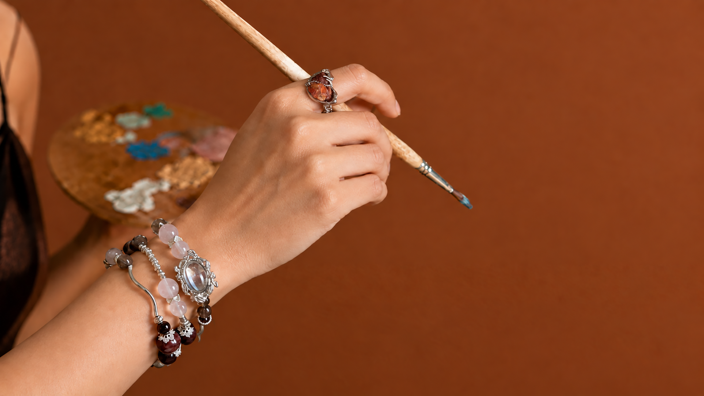 Hand wearing ON STUDIES natural stone bracelets and ring beside an artist’s palette